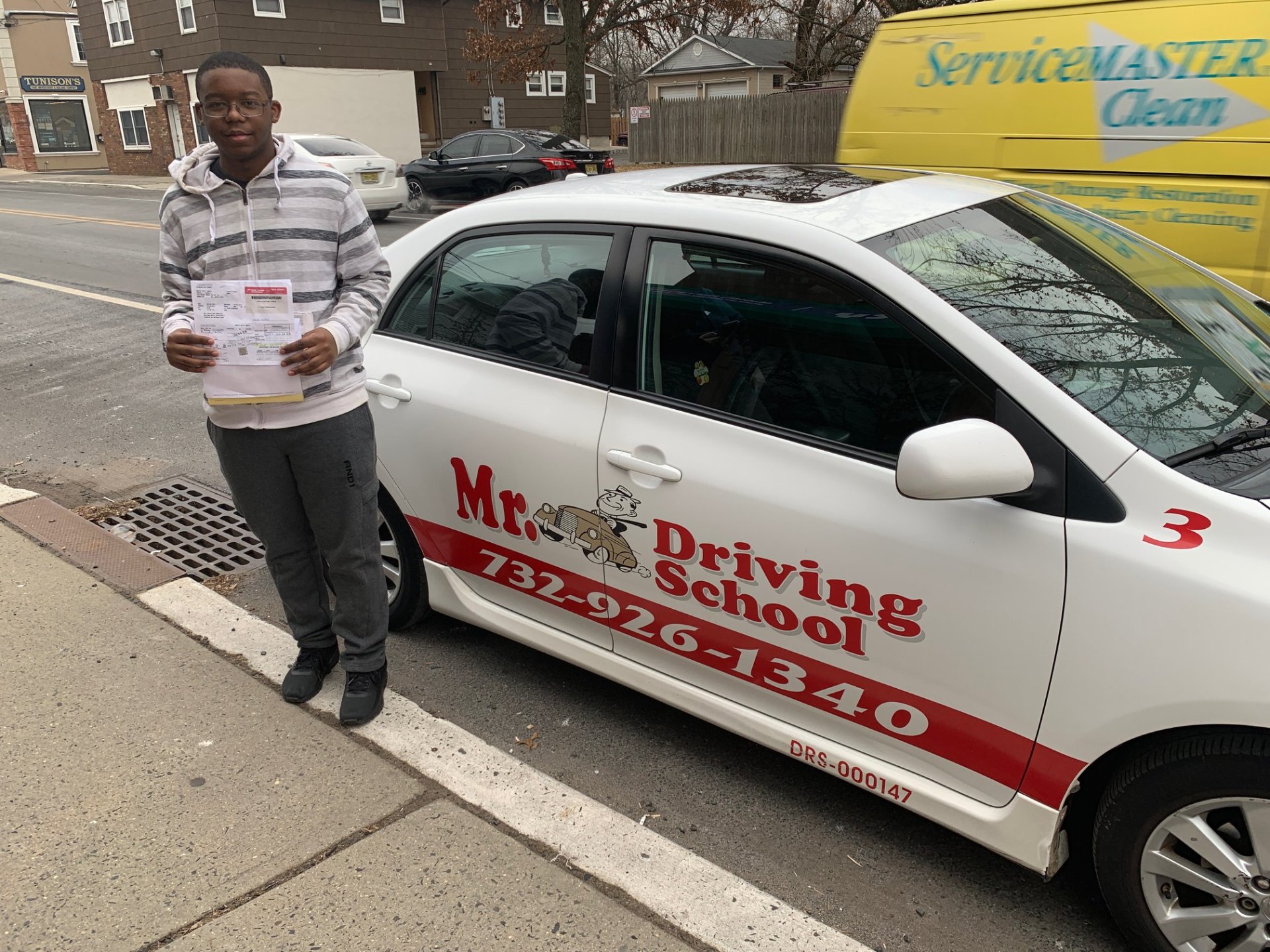 Student with papers next to driving school car
